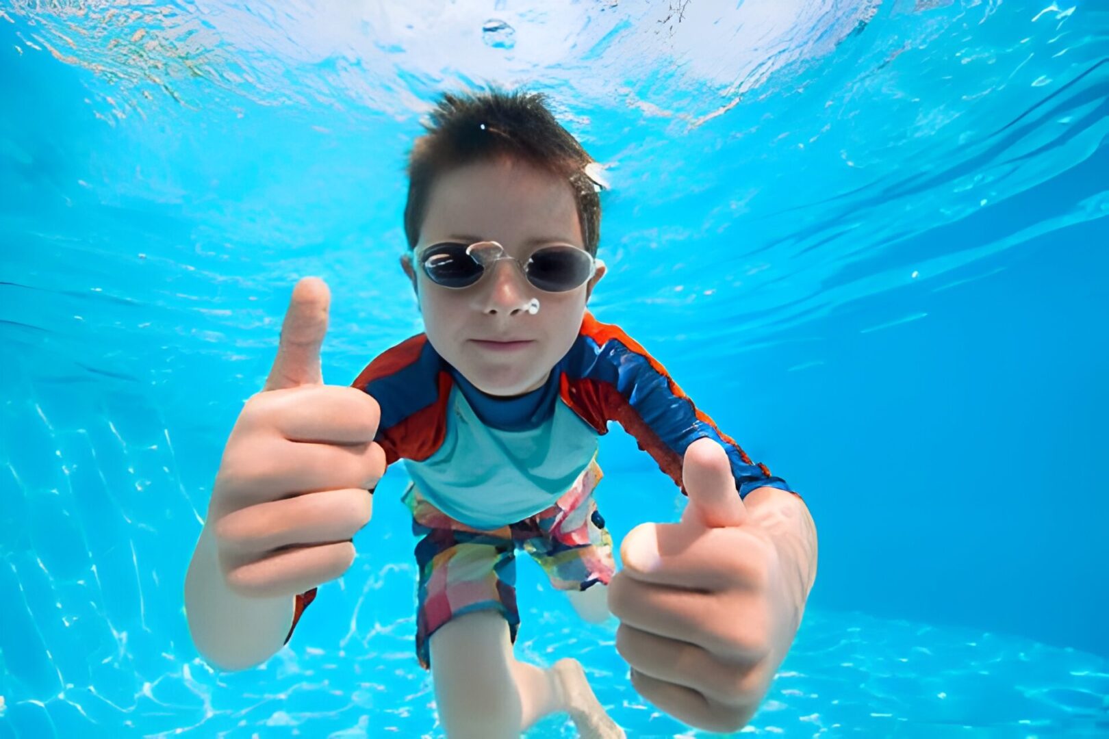 Child underwater giving thumbs up.
